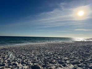 A beach with sand and water, a clear sky, and the sun.