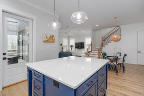 A modern kitchen with a central island, a dining area with blue chairs, and a staircase leading to an upper level.