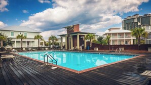 A swimming pool with a wooden deck, surrounded by palm trees and buildings. - Tigh Na Mara is a Porch Lover’s Paradise in Orange Beach, AL (Orange Beach)