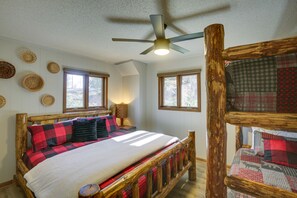 Een slaapkamer met een houten bedframe, een plafondventilator en meerdere ramen.