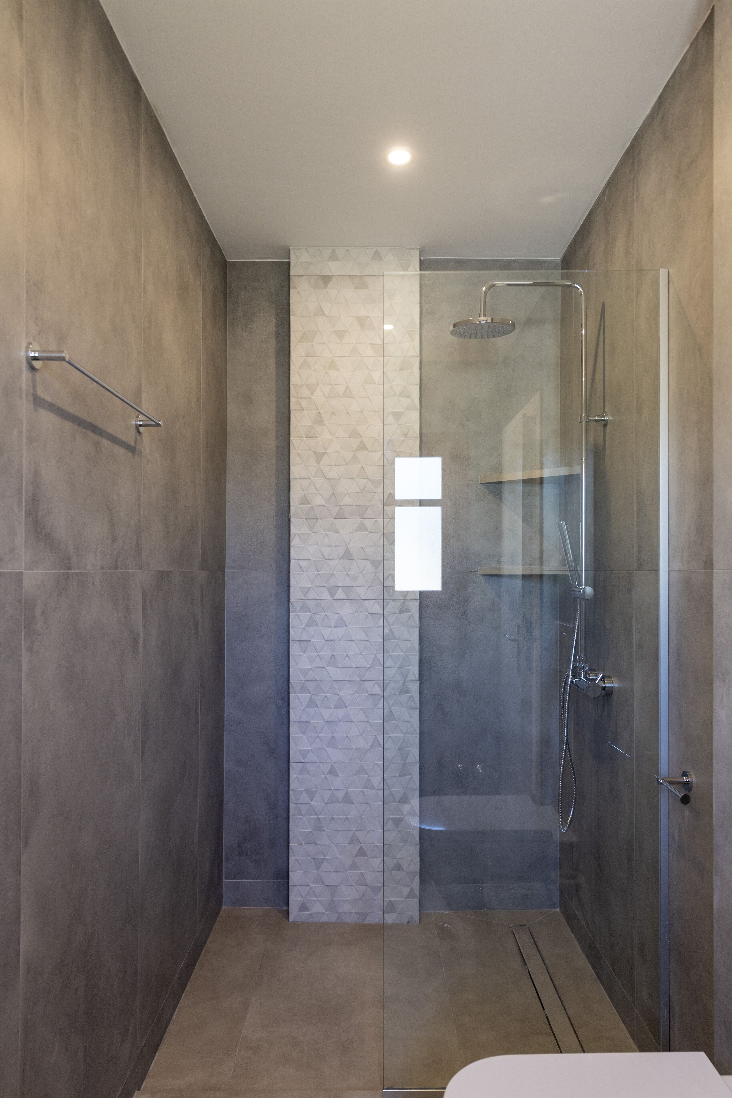 Eine moderne Dusche mit Glastür, einer vertikalen, strukturierten Wand und einer Metallhandstange.