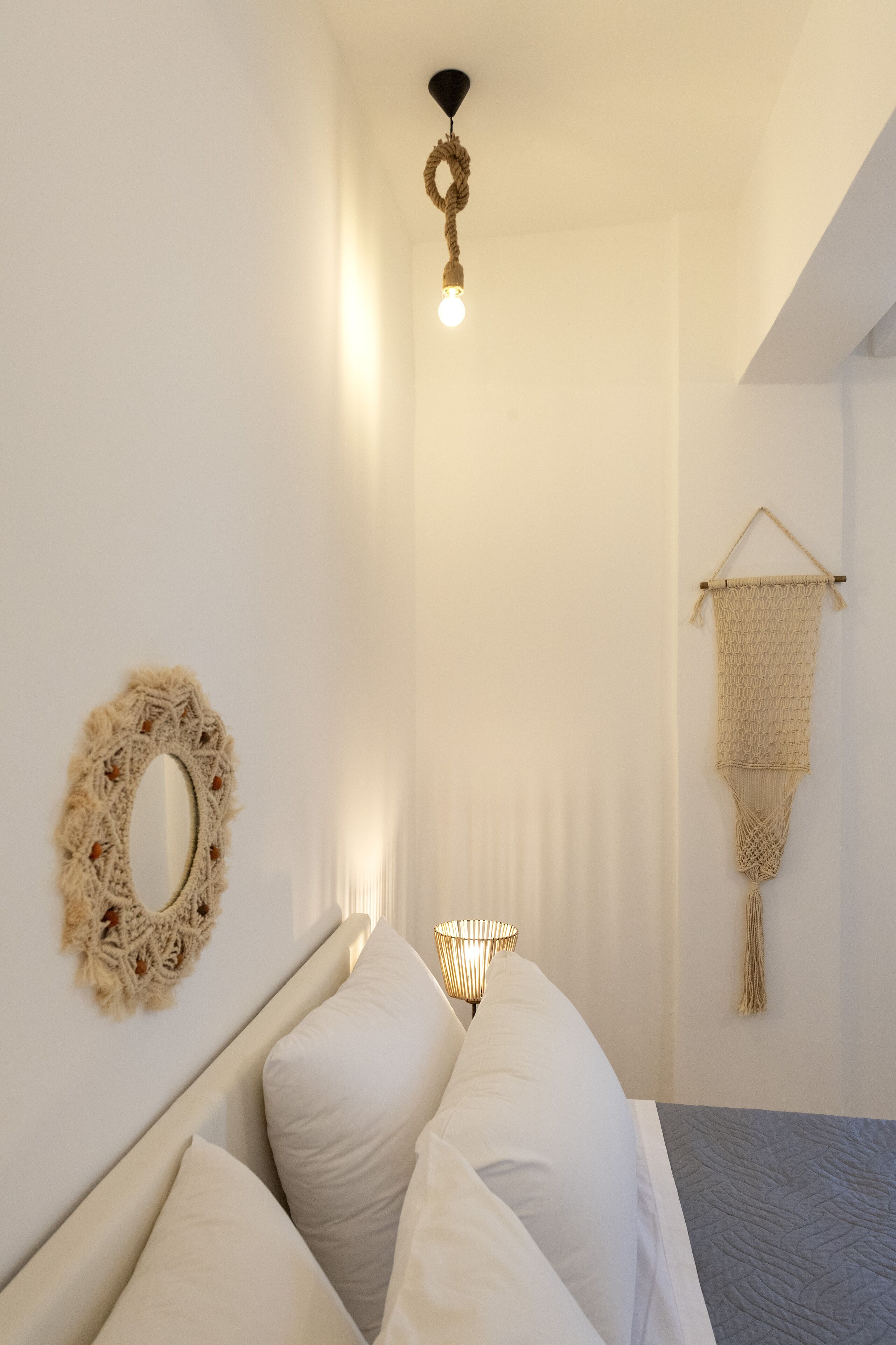 Una camera da letto con un letto, un pannello decorativo in macramè, uno specchio circolare e un lampadario.