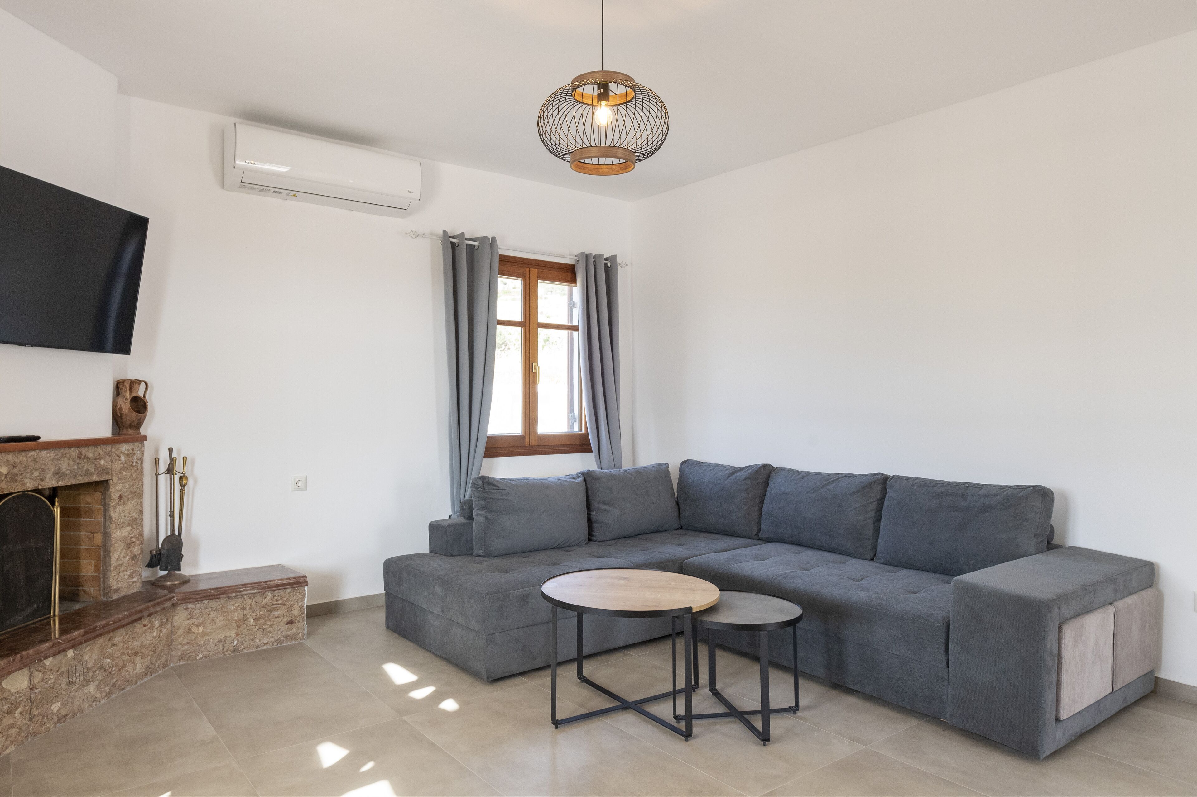 A modern living room with a grey sectional sofa, a small wooden table, a fireplace, and a large TV mounted on the wall.