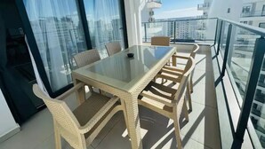 A balcony with a glass table and wicker chairs, overlooking a cityscape. - Amadeus Apartments in Caesar Resort&Spa,Long Beach.
 (Nicosia)