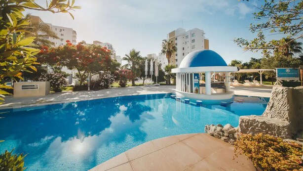 A swimming pool with a blue dome structure, surrounded by palm trees and other greenery. - Amadeus Apartments in Caesar Resort&Spa,Long Beach.
 (Nicosia)