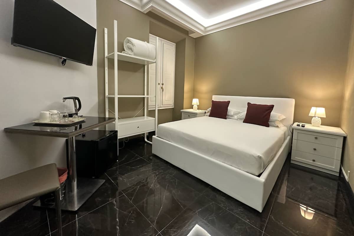 Una habitación de hotel moderna con una cama grande, un televisor de pantalla plana en la pared, una tocador con espejo y un escritorio pequeño con un hervidor.
