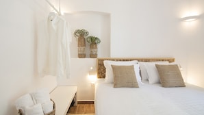Een slaapkamer met een bed, witte handdoeken, een mand met handdoeken en twee rieten vazen met planten.