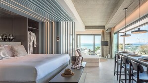 A modern hotel room with a large bed, a seating area with a view, and a dining space with bar stools. - Arca A1 Junior Suite (Athens)