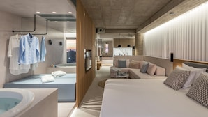 Una habitación de hotel moderna con una cama grande, una zona de estar con sofá y mesa de centro, un baño con bañera y vistas a la ciudad.