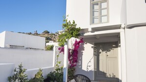 A white building with a stone patio, two black chairs, and a purple flowering plant.