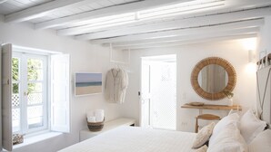 A bedroom with a large bed, a bedside table, a hanging rack, a mirror, and a window with an open door.