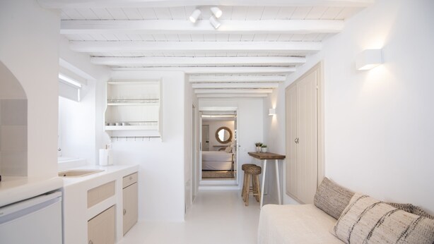 A modern, white-themed hallway leading to a bedroom with a bed and a small table.