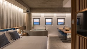 A modern bedroom with a large bed, a built-in desk, and a view of the sea through windows. - Porfyra B2 Master Suite (Athens)