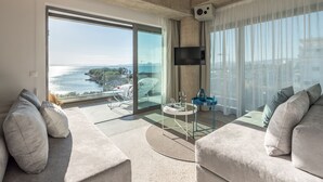 A modern living room with a large sliding glass door leading to a balcony, a flat-screen TV mounted on the wall, and a round coffee table. - Porfyra B2 Master Suite (Athens)