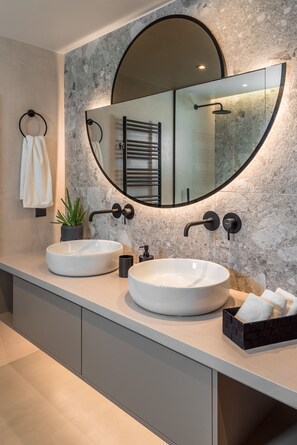 A modern bathroom with two round white sinks, a large mirror, and a potted plant.