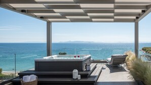 A hot tub with a view of the ocean, a wicker basket with towels, and a lounge chair.
