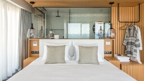 A modern hotel room with a large bed, a wooden headboard, a mirror, and a view of the sea.