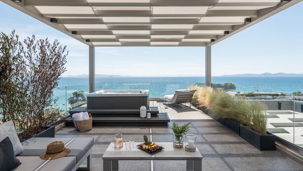 A rooftop terrace with a pool, lounge chairs, a table with drinks and fruit, and a view of the ocean.