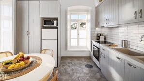 Cocina moderna con armarios blancos, un microondas y un lavamanos. Hay un frutero en la mesa y una ventana con vistas a edificios.