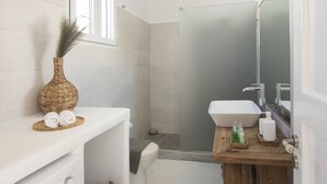 A modern bathroom with a washing machine, a wooden vanity, a glass shower enclosure, and a large mirror. - Pietra Bianca 1891 Junior Suite (Mykonos)