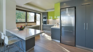 Een moderne keuken met een groot eiland, roestvrijstalen apparatuur en uitzicht op het groen.