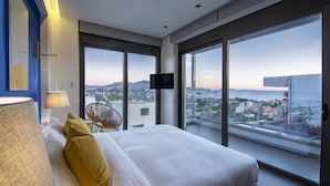Een moderne hotelkamer met een groot bed, een televisie en uitzicht op de stad door middel van kamerhoge ramen.