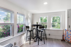 Een eethoek met een tafel en vier stoelen, grote ramen met zonwering en uitzicht op groen buiten.