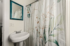 Een badkamer met een wit wastafelmeubel, een spiegel met een blauwgroene lijst en een douchegordijn met een bloemenprint.