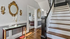 Un'ampia stanza con pavimento in legno, una scala con ringhiera nera e specchi dorati e decorati alle pareti.