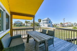 A wooden deck with a table and chairs, a yellow awning, and a view of houses in the background.