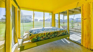 Ein Zimmer mit einem Hängeschaukelbett, großen Fenstern und Blick ins Freie.