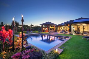 Ein Pool mit umlaufendem Garten, Sitzgelegenheiten im Freien und ein Gebäude mit überdachter Terrasse.