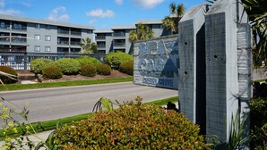 A sign for Sea Cabin Cherry Grove, a multi-story building with balconies and a landscaped area with bushes and small trees. - Cute condo rental at family-friendly resort - secluded condos with pool (North Myrtle Beach)