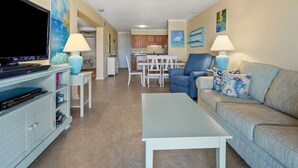 A living room with a flat-screen TV, a sofa, a coffee table, and a dining area with a table and chairs. - Cute condo rental at family-friendly resort - secluded condos with pool (North Myrtle Beach)