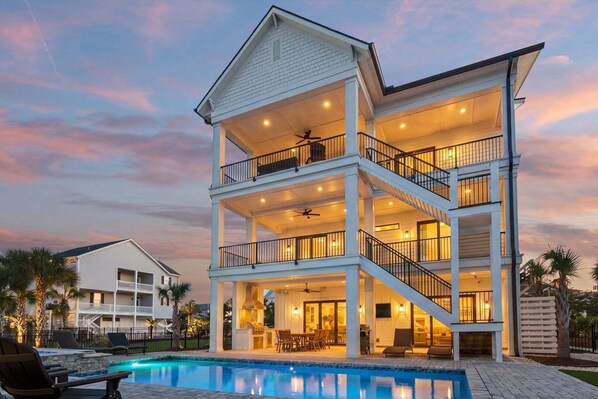 A multi-story house with a pool, balconies, and outdoor lighting.