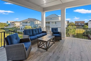 A covered balcony with wicker furniture, a wooden table, and a view of residential buildings.