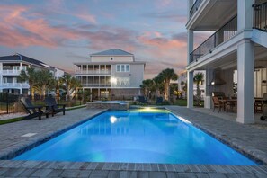 A swimming pool with lounge chairs, a barbecue area, and a large building with balconies in the background.