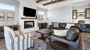 Ein Wohnzimmer mit Kamin, einer Couch, einem gestreiften Sessel, einem Couchtisch und einem Fernseher.