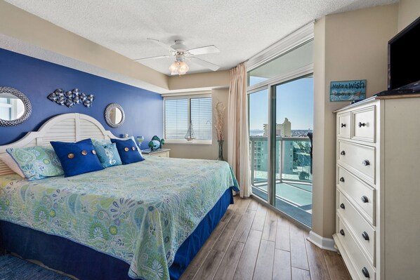 Une chambre dotée d’un grand lit, d’une commode, d’un ventilateur de plafond et offrant une vue sur la ville depuis un balcon.
