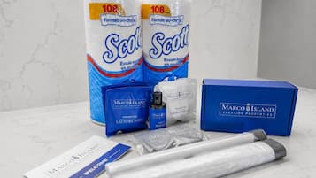 A set of toiletries including two rolls of Scott toilet paper, a blue Marco Island branded box, a welcome card, and a set of laundry pods.