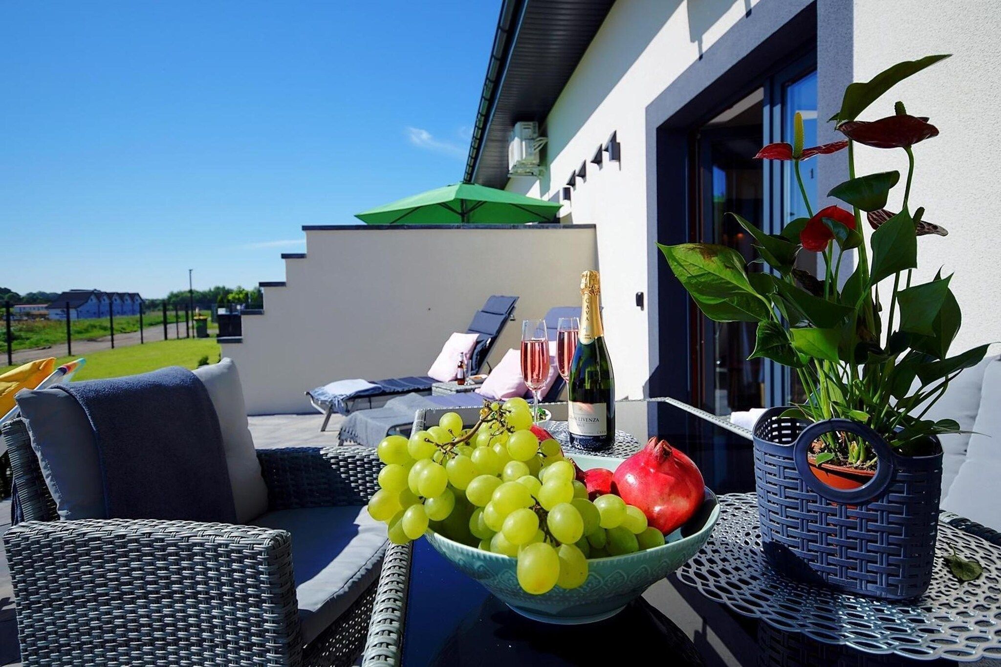 A balcony with wicker furniture, a bowl of fruit, a bottle of champagne, and a potted plant.