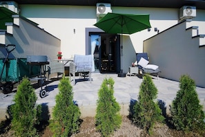 An outdoor patio with a table, chairs, a green umbrella, and a small garden with coniferous plants. - Holiday homes with terraces, Mielenko (Mielenko)