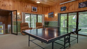 A ping pong table in a room with wooden walls and large windows. There are two chairs and a small table with a vase of flowers. - Cozy Condo at The Seasons Resort – Perfect for Skiing, Hiking & Family Fun 🎿❄️🏂🌲🗻 (Bartlett)
