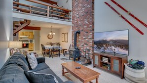 A cozy living room with a fireplace, a TV, and a loft area with a kitchen. - Cozy Condo at The Seasons Resort – Perfect for Skiing, Hiking & Family Fun 🎿❄️🏂🌲🗻 (Bartlett)