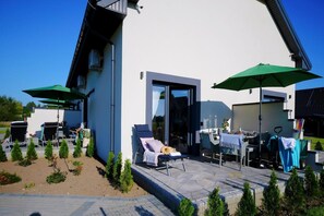 A modern outdoor patio with lounge chairs, umbrellas, and a small garden. - Comfortable and spacious holiday home, Mielenko (Mielenko)