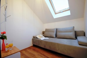 A small, modern room with a sofa, a small table with a vase and glasses, and a skylight above the sofa.