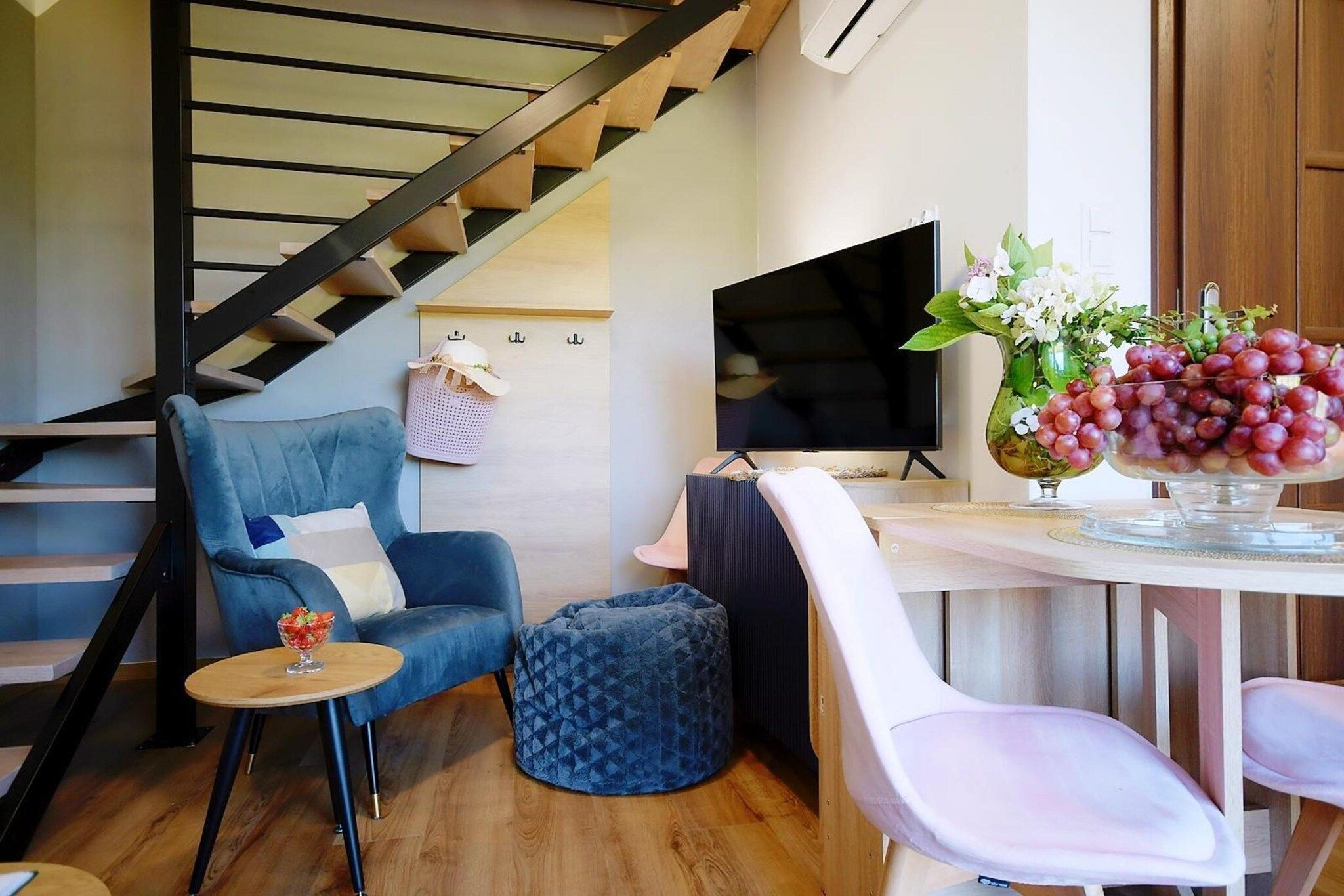 A modern living space with a staircase, a blue sofa, a small round table, a white chair, and a vase with flowers.