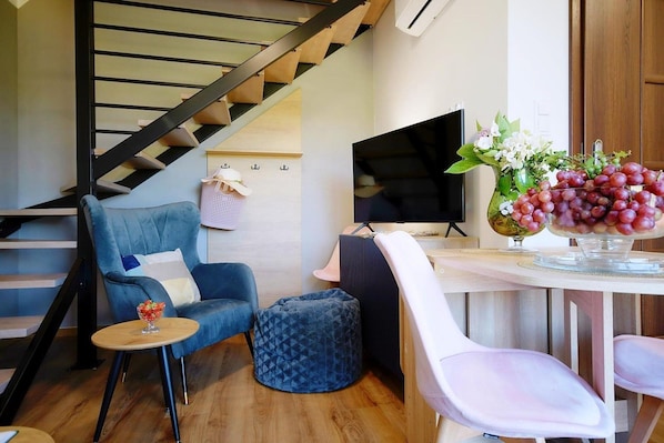 A modern living space with a staircase, a blue sofa, a small round table, a white chair, and a vase with flowers.