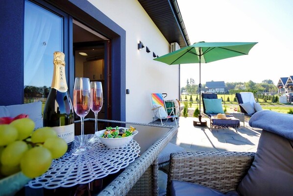 An outdoor seating area with a table set for two, a bottle of wine, glasses, and a bowl of salad.