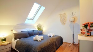 A bedroom with a skylight, a bed with a dark quilt, a bedside table with a lamp, and a nightstand.